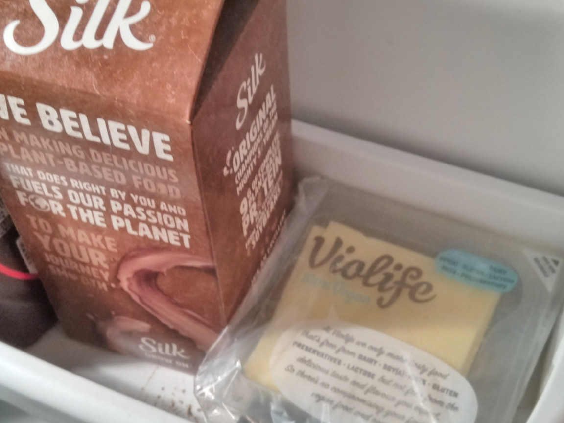A package of cheese sitting in a refrigerator next to some chocolate soy milk